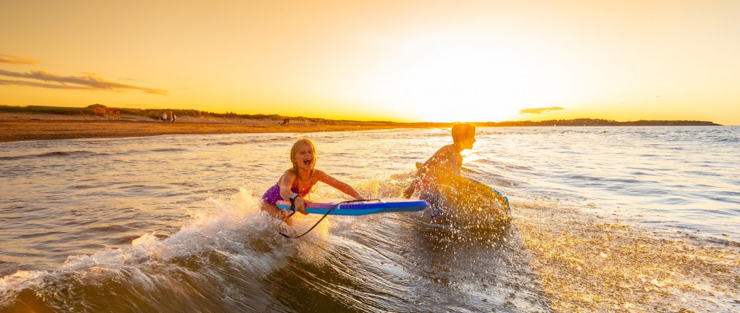 Two children play on boogies boards in surf at sunset